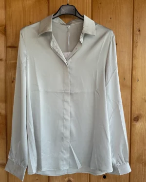 Lichtgrijze blouse van Sweet Miss Women’s Fashion met kraag en verborgen knoopsluiting. Elegant, tijdloos en perfect voor zakelijk en casual