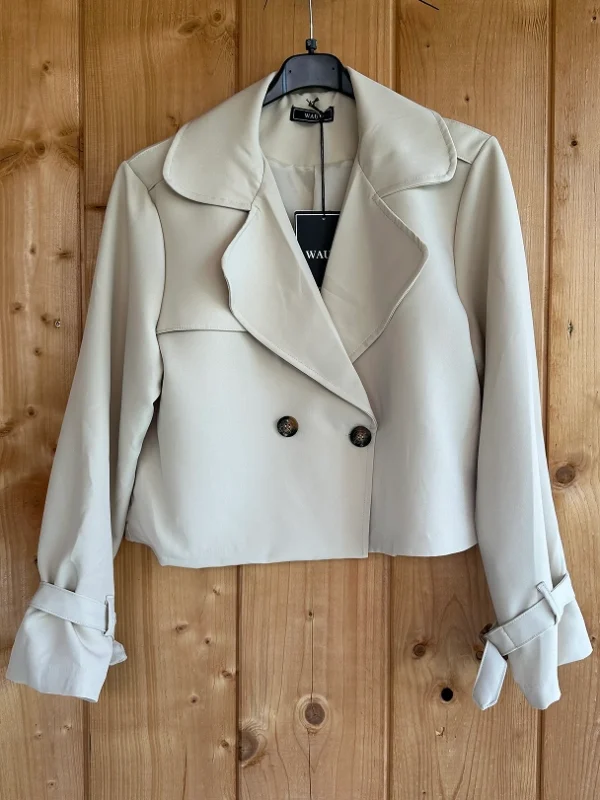 Stijlvolle beige cropped trenchcoat van Wauw Fashion. Met dubbele knopen en ceintuurdetails bij de mouwen. Tijdloos, elegant en veelzijdig te combineren.
