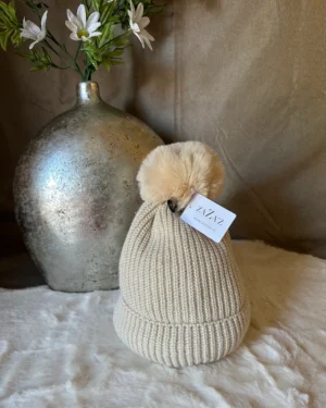 Crèmekleurige gebreide muts van Zaza’s met zachte beige pompon van imitatiebont, stijlvol en warm voor de winter.