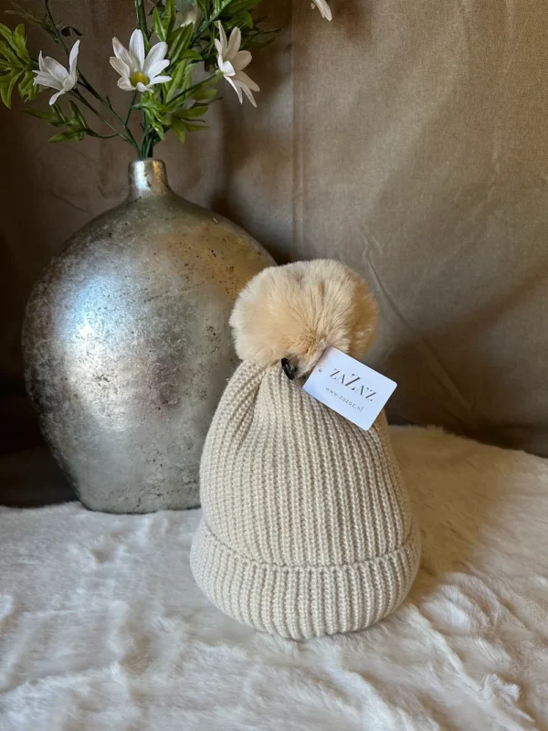 Crèmekleurige gebreide muts van Zaza’s met zachte beige pompon van imitatiebont, stijlvol en warm voor de winter.