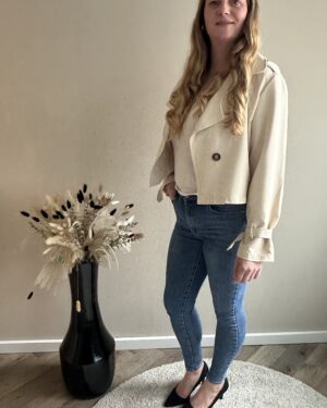 Stijlvolle beige cropped trenchcoat van Wauw Fashion. Met dubbele knopen en ceintuurdetails bij de mouwen. Tijdloos, elegant en veelzijdig te combineren.