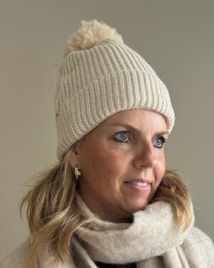 Crèmekleurige gebreide muts van Zaza’s met zachte beige pompon van imitatiebont, stijlvol en warm voor de winter.
